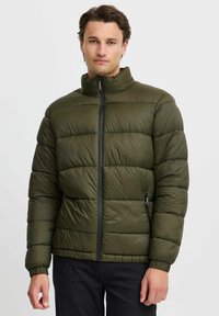 Oliven grønn dunjakke med ståkrage, frontglidelås og elastiske mansjetter. Har et kviltet design og sidelommer med glidelås.
