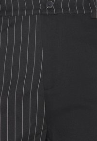 Pantalon noir à motif rayures fines. Confectionné en tissu lisse, avec une fermeture standard par bouton et des poches latérales.