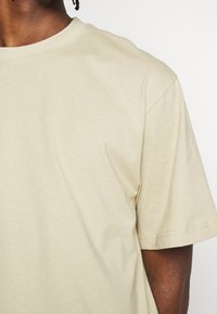 Beige T-shirt lavet af blødt bomuld, med rund hals og korte ærmer. Glat tekstur med pænt syede sømme.