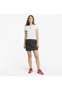 Camiseta blanca con logo negro, pantalones cortos negros con cintura elástica y zapatillas deportivas rojas. Diseño simple y estilo atlético casual.