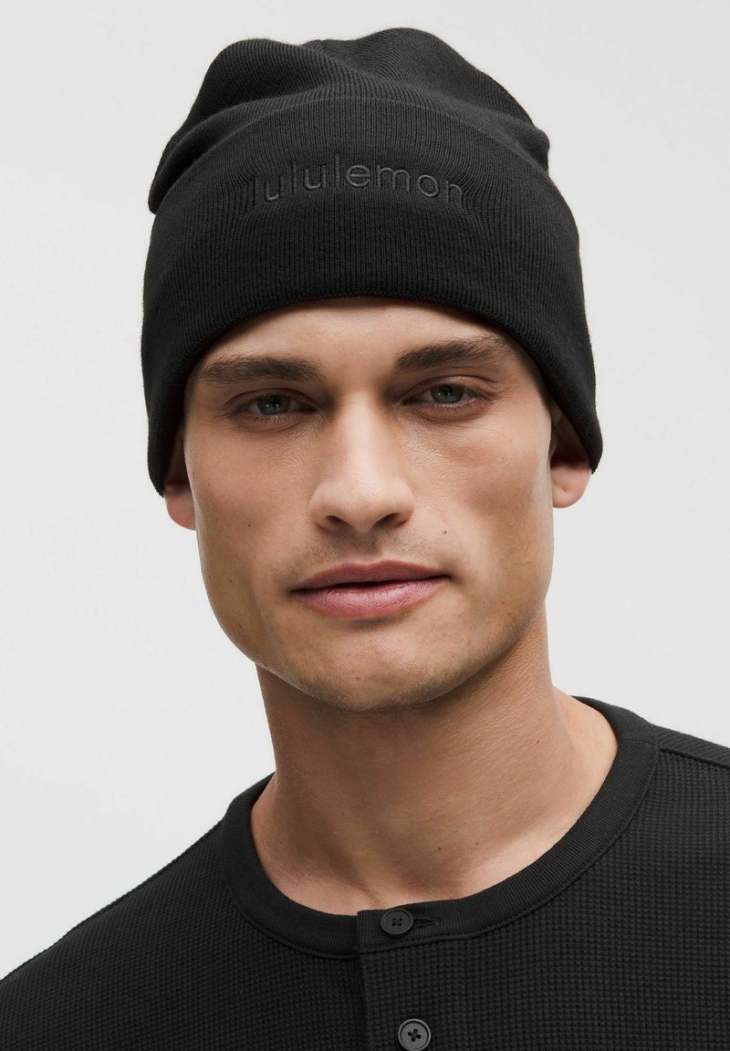 Czarna dzianinowa czapka beanie o luźnym kroju, z delikatnym wytłoczonym logo. Gładka tekstura i miękki materiał zapewniają ciepło i komfort.