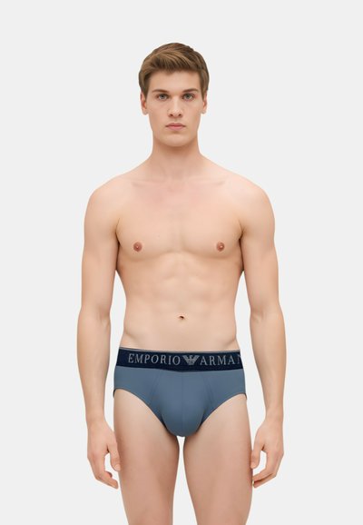 Slip da uomo in tessuto grigio opaco, con elastico blu navy e logo "Emporio Armani". Texture liscia e design aderente.