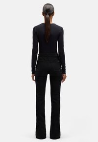 Czarne jeansy z rozszerzanymi nogawkami i wysokim stanem, wyposażone w tylne kieszenie i gładką, teksturowaną tkaninę. Połączone z dopasowaną czarną bluzką z długim rękawem.
