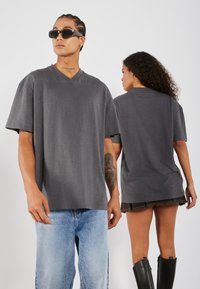 Sivý oversized V-krčný tričko s krátkymi rukávmi, s hladkou textúrou. Model nosí svetlomodré džíny a iný model má na sebe krátku sukňu.