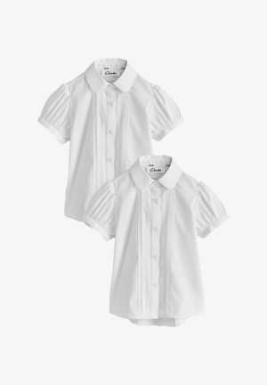 Deux blouses blanches pour enfants à manches courtes avec manches bouffantes, boutonnage devant, cols arrondis et plis décoratifs verticaux.
