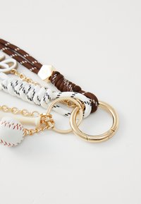 Set privjesaka za ključeve s pletenim bijelim i smeškim šnjurima, dva zlatna metalna prstena i malim privjeskom u obliku baseball lopte s crvenim šavovima.