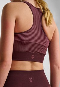 Bordeaux geribbelde sportbeha met een brede band, voorzien van een subtiel logo. Materiaal heeft een gestructureerde afwerking en het ontwerp omvat een racerback-stijl.