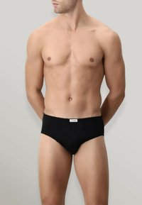 Brief per uomo nero con una texture liscia, elastico in vita e un piccolo etichetta sul davanti. Taglio classico senza motivi o accenti visibili.