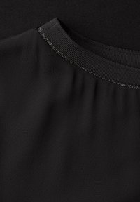 Indumento nero caratterizzato da un tessuto liscio e strutturato con scollo a coste. Presenta un leggero scintillio lungo il bordo del colletto.