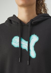 Sweat à capuche noir avec un design de logo abstrait turquoise vif. Tissu texturé avec cordons de serrage et embouts métalliques.