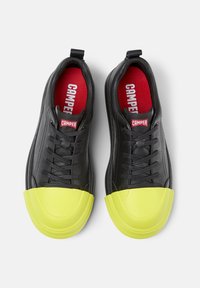 Schwarze Leder-Sneaker mit einer abgerundeten gelben Gummikappe, ausgestattet mit roten Innensohlen und einem Logotag an der Zunge, Schnürdesign für eine gute Passform.