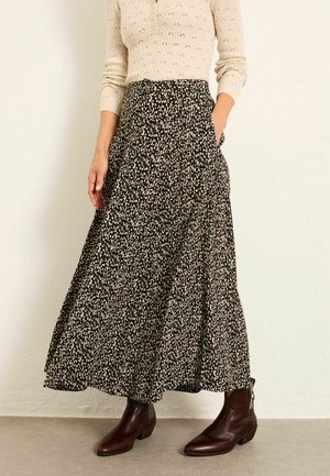 Maxirock mit schwarzem und cremefarbenem Muster, fließendem Design, hoher Taille und Taschen, kombiniert mit braunen Stiefeletten.