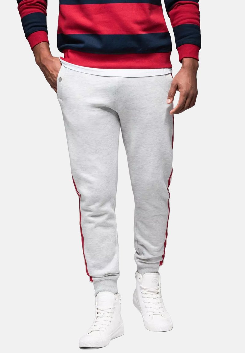 Graue Sweatpants mit roten Seitenstreifen, aus weichem Stoff gefertigt. Das Design umfasst seitliche Taschen und gerippte Bündchen an den Knöcheln.