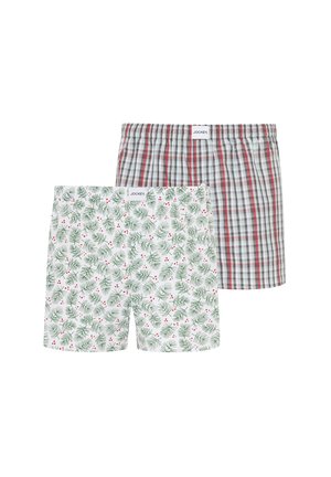 Two pairs of Jockey brand men's boxer shorts, one with green pine branch and red berry print, the other with red and gray plaid pattern.