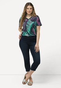 Top multicolore con stampa di foglie tropicali in verde e rosa, abbinato a pantaloni cropped in denim scuro e sandali argentati.