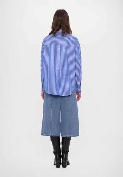 Blue and white striped shirt with a relaxed fit and button-up back, paired with wide blue denim culottes and black knee-high boots.
