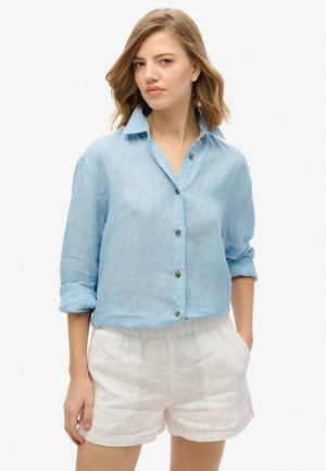 Lichtblauw, knoopsluiting linnen shirt met opgerolde mouwen, voorzien van een kraag en textuurstof. Gecombineerd met witte, elastische shorts met tailleband.