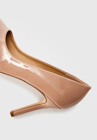 Decolleté in pelle laccata nuda con punta affusolata e sottile tacco a stiletto. Texture liscia e design minimalista.