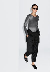 Szara i biała w paski koszula z długim rękawem, czarne luźne spodnie, czarny dzianinowy szal i czarne buty wsuwane. Gładkie faktury, swobodny design.