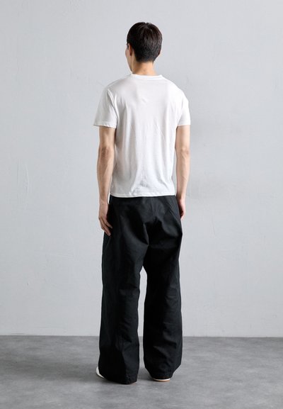 White cotton t-shirt and loose black pants with a matte texture, viewed from the back. Clean lines and casual fit highlighted.
