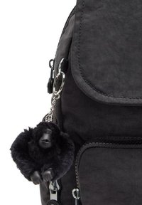 Black fabric backpack featuring a front flap, zippered compartments, and a plush black gorilla keychain attached with a silver chain.