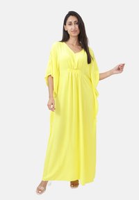 Robe maxi jaune avec un décolleté en V, des manches courtes et une taille cintrée. Tissu léger avec une texture lisse. Association avec des sandales transparentes.
