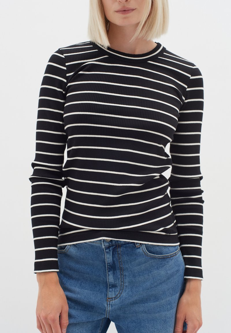 Svart och vit randig ribbad långärmad tröja med rundad halsringning, ihop med ljusblå denimjeans.