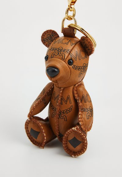 Bruin leren sleutelhanger in de vorm van een teddybeer met gestikte randen, zwarte logo-patronen, en een gouden metalen ring en clip aan de bovenkant bevestigd.