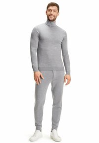 Maglione a collo alto in morbido tessuto grigio e pantaloni affusolati coordinati, con una sottile texture e linee pulite, abbinati a scarpe da ginnastica bianche.