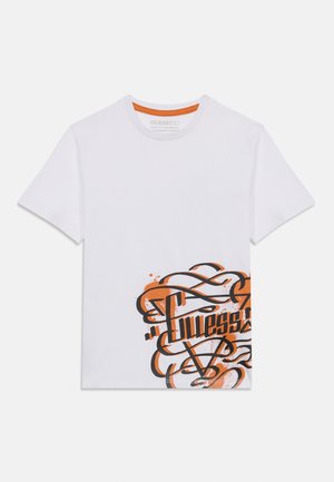 T-shirt blanc à manches courtes avec un logo "Guess" en style graffiti orange et noir, situé sur le bas à droite de l'avant.