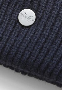 Tessuto a coste blu navy con un bottone rotondo in argento che mostra il testo inciso "PEARLWOOD" e linee decorative. Texture morbida e trama densa.