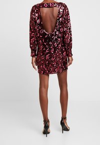Robe à sequins avec un motif léopard en tons rouges et roses. Elle présente des manches longues et une silhouette dos décolleté profond.
