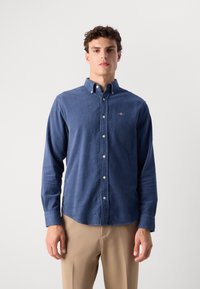 Langarm overhemd van donkerblauwe katoen, met een klassieke kraag, voorzakken en een klein geborduurd logo op de borst.