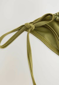 Top bikini verde oliva con una texture liscia, caratterizzato da un dettaglio annodato e cuciture piatte per una vestibilità sicura. Accenti di paillettes lungo il bordo.