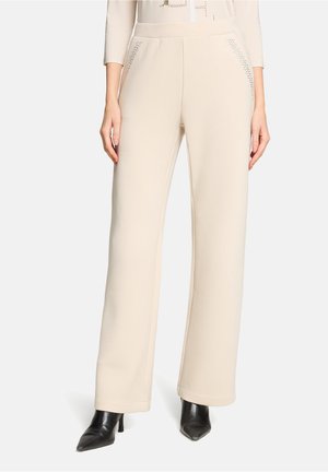 Beige wijde broek met een gladde textuur, voorzien van zijzakken met subtiele gestuifde accenten, gecombineerd met zwarte pumps met spitse neus.