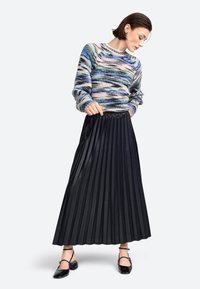 Gebreide trui met meerkleurige strepen, gecombineerd met een lange zwarte plissérok. Zwarte schoenen met enkelbandjes maken de outfit compleet.