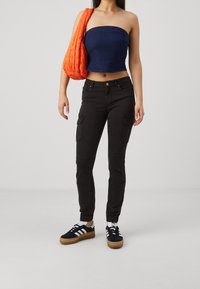 Zwarte cargobroek met taps toelopende manchetten, gecombineerd met een marineblauw strapless top. Een gestructureerde oranje tas en zwarte sneakers met witte strepen maken de look compleet.