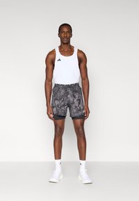 Ανδρική αθλητική στολή που περιλαμβάνει λευκό αμάνικο μπλουζάκι και μαύρα σορτς με μοτίβο και ελαστική μέση. Περιλαμβάνει λευκά αθλητικά παπούτσια και κάλτσες.