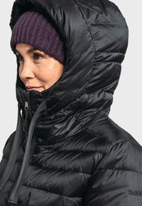 Schwarze Pufferjacke mit hohem, gepolstertem Kragen und grauen Kordeln. Getragen mit einer gerippten lila Mütze, die eine glatte, glänzende Oberfläche hat.