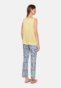 Yellow satin sleeveless top, loose fit, rounded neckline. Accompanied by patterned trousers in blue, green, and beige. Pink flat shoes.