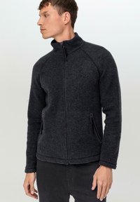 Veste en polaire gris foncé avec un col haut, fermeture éclair à l'avant et deux poches latérales. Présente des manches raglan et un tissu doux et texturé.