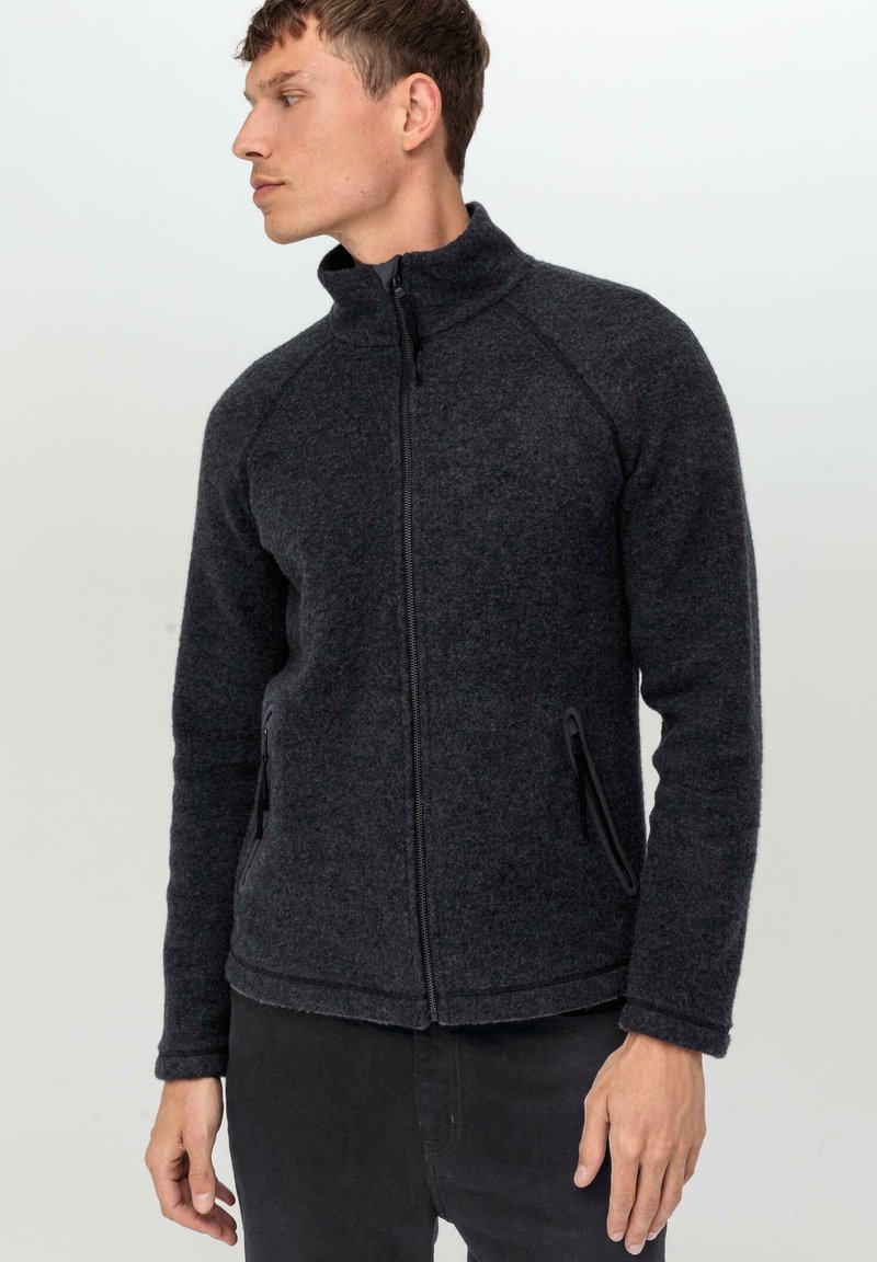 Veste en polaire gris foncé avec un col haut, fermeture éclair à l'avant et deux poches latérales. Présente des manches raglan et un tissu doux et texturé.