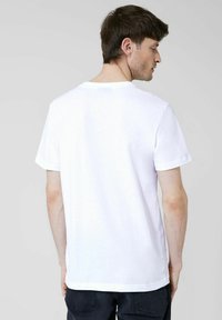Camiseta de algodón blanca de manga corta, con escote redondo y un diseño trasero liso. No hay gráficos ni patrones visibles.