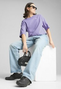 Maglietta corta viola, jeans a gamba larga azzurri, sneakers nere con punte e una piccola borsa nera con il logo "PUMA". Occhiali da sole neri.