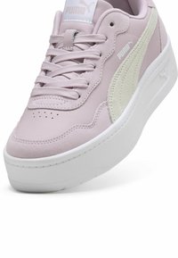 Ružičaste nubuk tenisice s bijelim teksturiranim detaljima, okrugli vrh, vezivanje sprijeda i debeli bijeli potplat. Puma logo vidljiv na jeziku i sa strane.