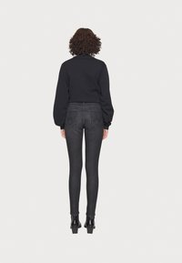 Suéter corto negro combinado con jeans ajustados gris oscuro. El material parece suave; los jeans tienen bolsillos traseros y un diseño ajustado.