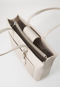 Beige tote bag made from synthetic material, featuring two straps, a zipper pocket, and an interior organization sleeve. Textured front panel.