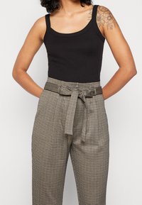 Černý ribovaný top bez rukávů v kombinaci s vysokými kalhotami s texturou a kostkovaným vzorem, které mají pás s vázáním a boční kapsy.