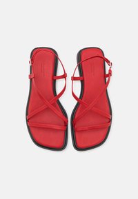Røde flate sandaler med minimalistisk design. Har tynne, kryssende stropper og en svart såle. Teksturert fotseng for komfort.