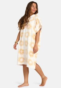 Poncho con capucha en suave tejido de rizo con un patrón de sol en tonos dorados sobre un fondo crema, con aberturas laterales para mayor movilidad.